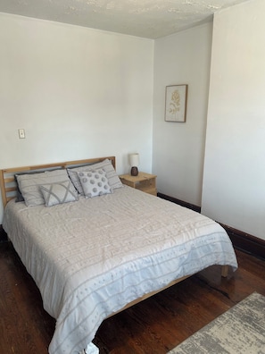 A bedroom with a bed, bedside table, lamp, and a framed picture on the wall.
