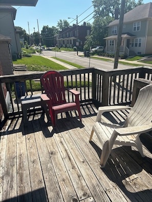 A wooden deck with two Adirondack chairs, a railing, and a view of a residential street.