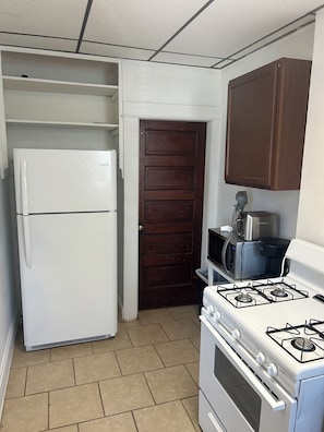 A kitchen with a white refrigerator, a stove, a microwave, and a dark wooden door.