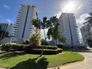 A residential building complex with multiple high-rise apartments, a well-maintained lawn, and a few palm trees. - CB12-Ocean front corner unit (Carolina)