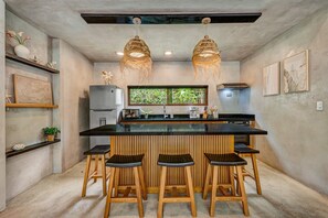 Une cuisine compacte dotée d’un îlot central, de tabourets de bar, de luminaires suspendus et d’un réfrigérateur.