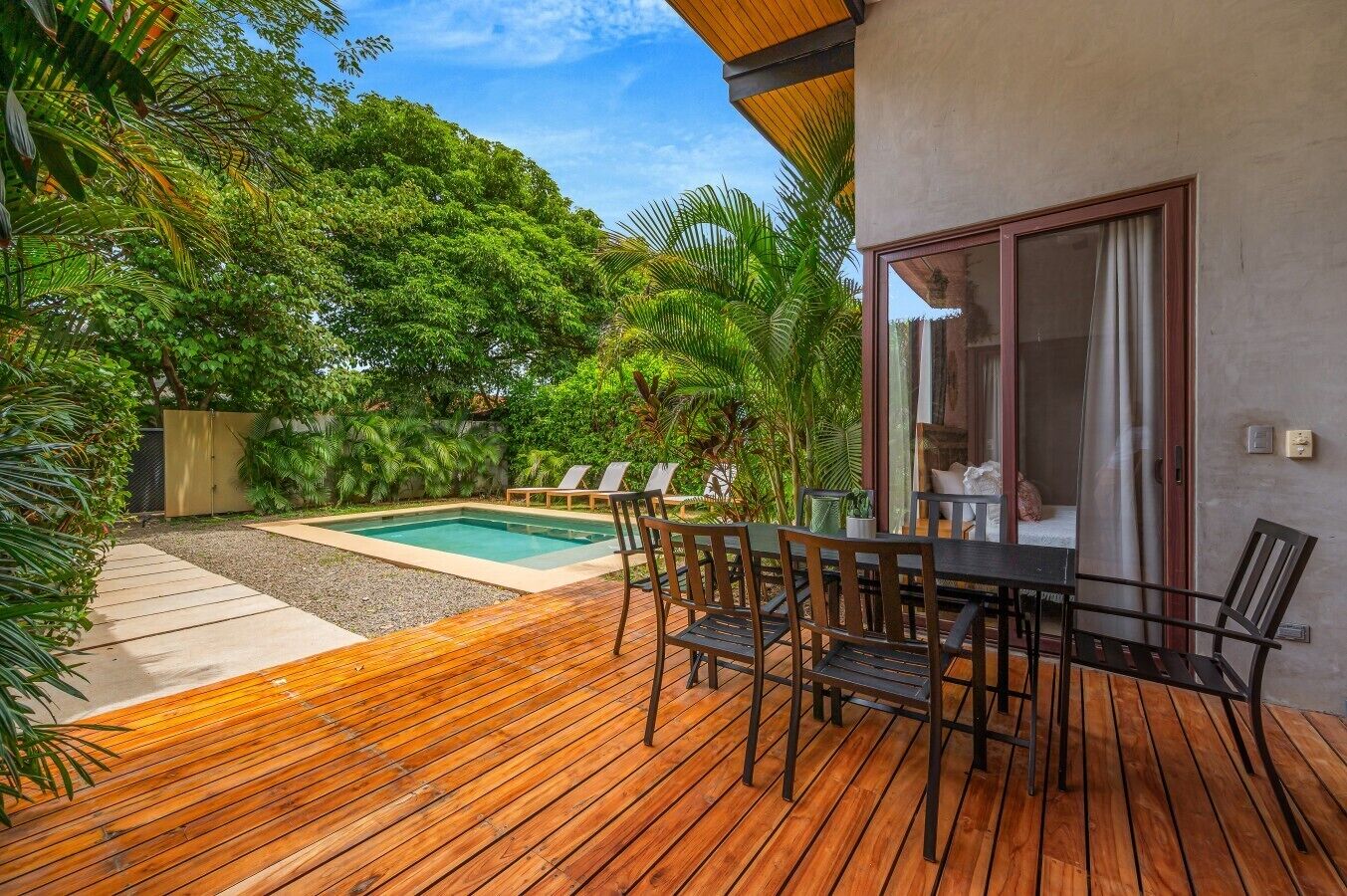 A wooden deck with a pool and lounge chairs, surrounded by lush greenery.