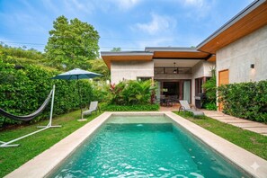 Ein modernes Haus mit Swimmingpool, Gartenmöbeln und üppiger Bepflanzung.