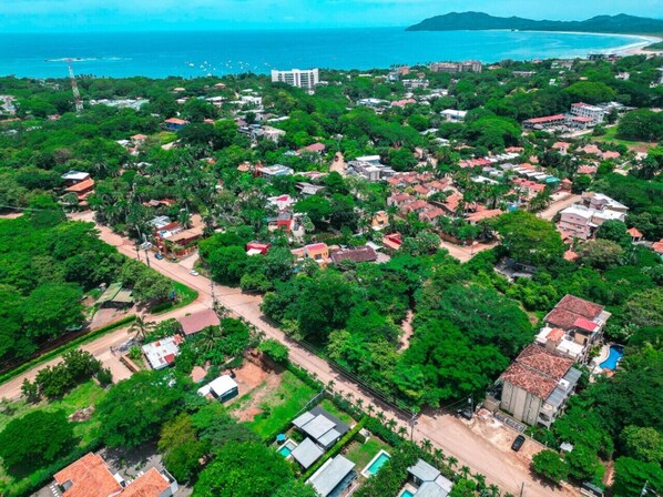 An aerial view of a coastal town with dense greenery, residential buildings, and a visible beach. - Modern Jungle Retreat w/ Detached Guest Home Near Beach (Tamarindo)
