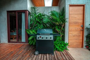 Ein Grillplatz im Innenhof mit Holzterrasse, einer Schiebetür und einer Betonwand.