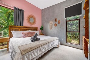 A bedroom with a large bed, a window with a view of greenery, a wooden headboard, and a wall-mounted mirror. - Modern Jungle Retreat w/ Detached Guest Home Near Beach (Tamarindo)