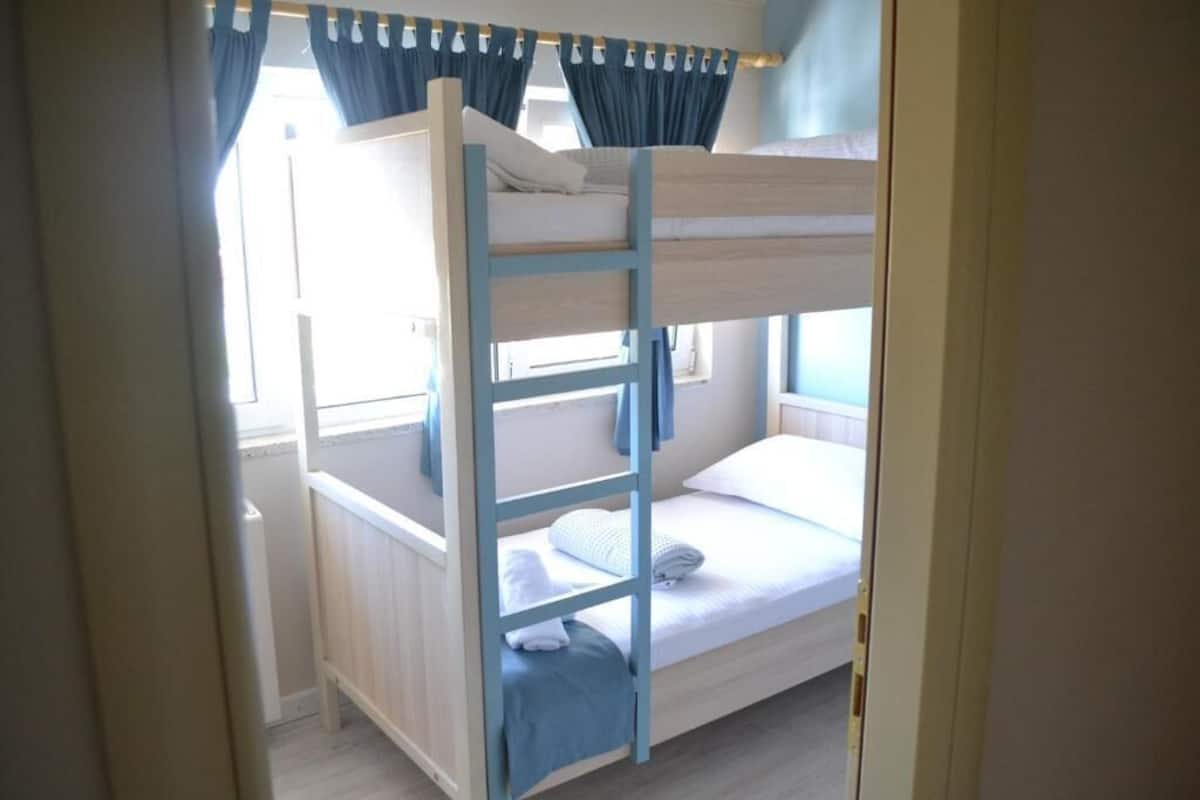 Dormitorio con literas, ventana, cortinas y puerta.