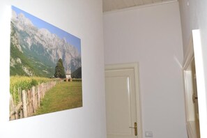 A room with a door, a wall-mounted picture of a mountainous landscape, and a small window. - Open Doors Bed & Breakfast  (Shkodër)