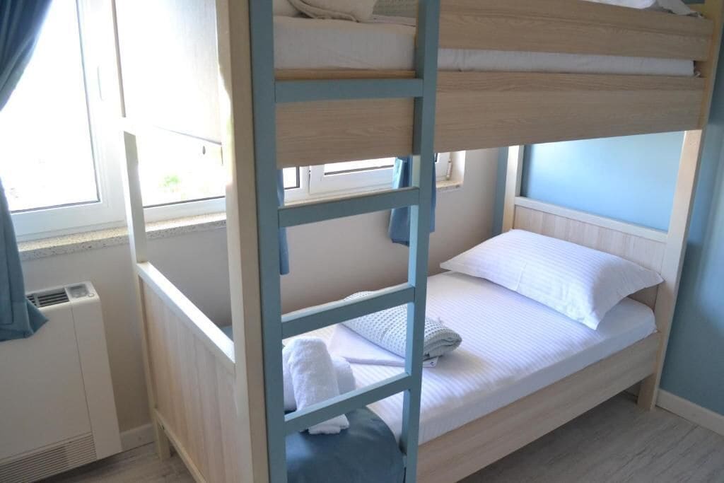 Una cama litera con escalera, una ventana con cortinas y un radiador.