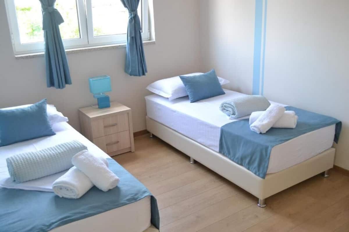 Un dormitorio con dos camas, una mesita de noche y un ventanal con cortinas.