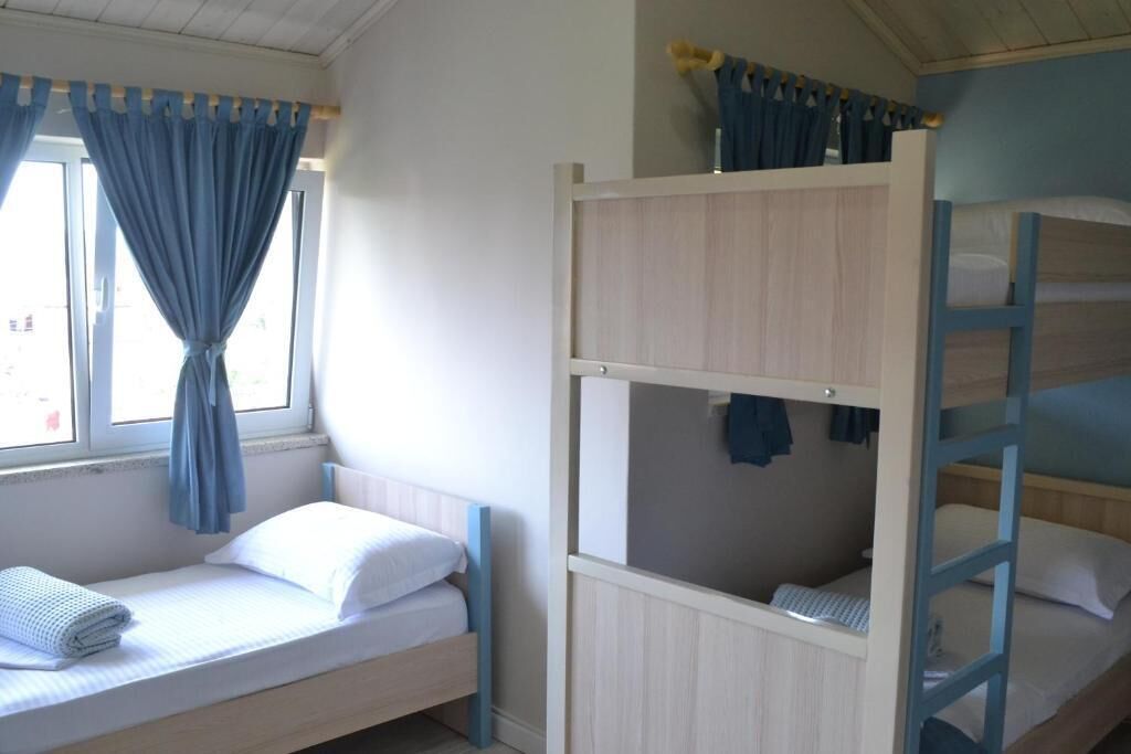 A bunk bed room with a window, curtains, and a bed with a rolled towel.
