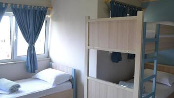 A bunk bed room with a window, curtains, and a bed with a rolled towel.