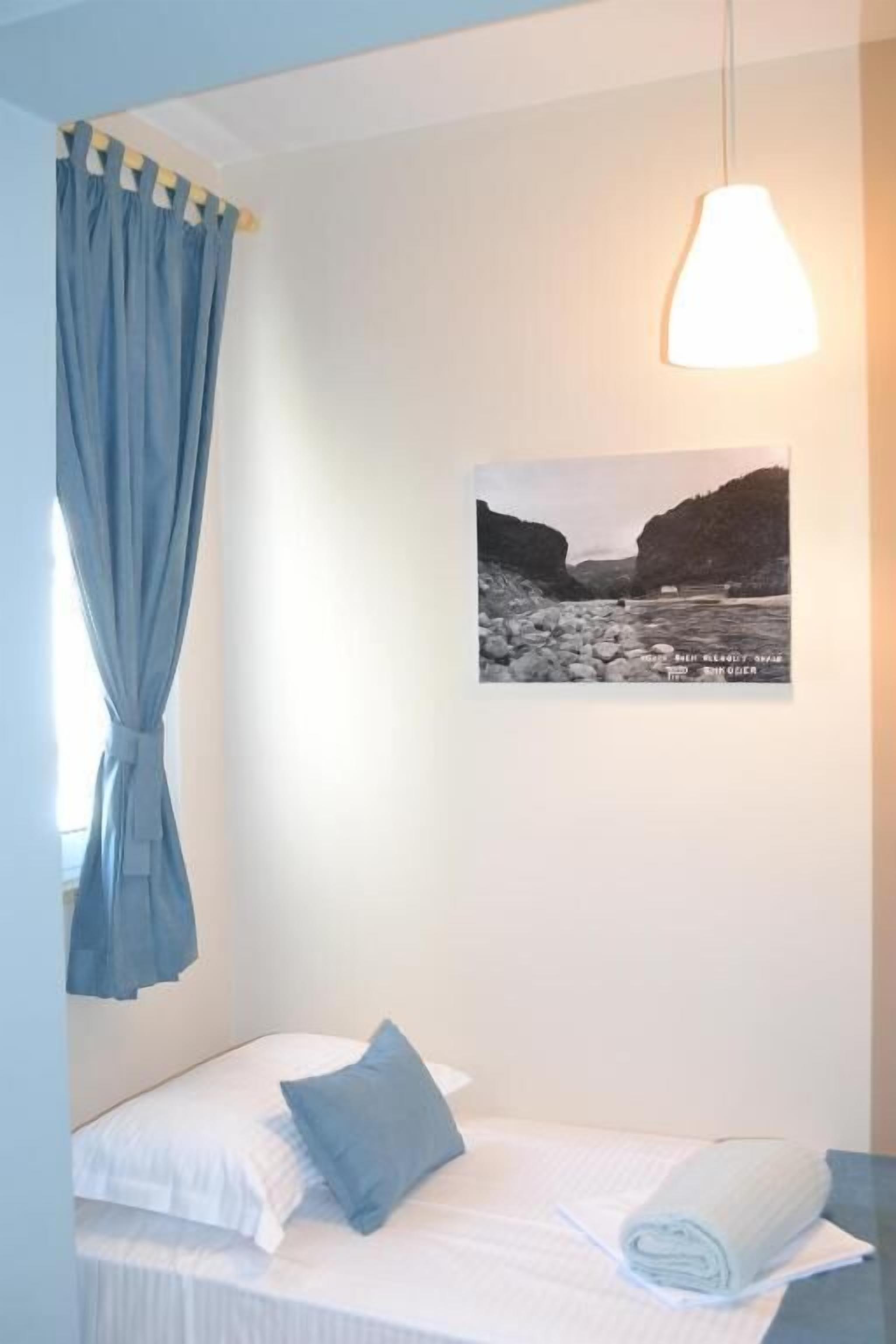 A bedroom with a bed, a blue curtain, a wall-mounted lamp, and a black and white photograph.