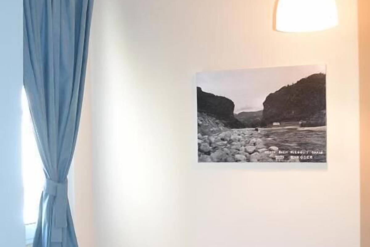 Un dormitorio con cama, cortina azul, lámpara de pared y fotografía blanco y negro.