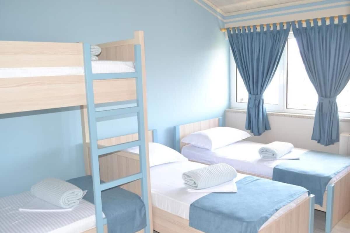 Una habitación con literas, una ventana con cortinas y una escalera de madera.