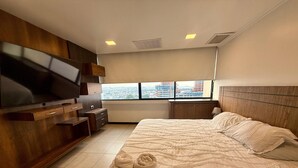 Ein Hotelzimmer mit einem Bett, einem Fernseher, einem Fenster mit Blick auf die Stadt und einem Holzschrank.