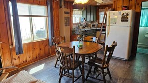 Un interior de madera con una mesa de comedor, sillas, un ventilador de techo y una zona de cocina con electrodomésticos.