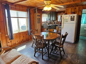 Un intérieur en bois comprenant une table à manger, des chaises, un ventilateur de plafond et un coin cuisine équipé d’appareils électroménagers.