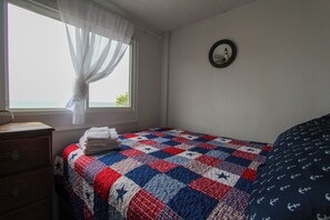 A bedroom with a bed, a dresser, a window with curtains, and a wall clock. - A spacious 3-bedroom cottage with real Lake Huron views and shared beach access just steps away. (Iosco County)