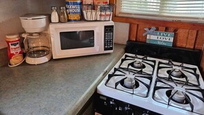 Una cocina con estufa, microondas y diversos utensilios.