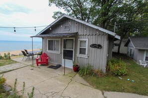A small, single-story cabin with a porch, a red chair, and a potted plant. - A spacious 3-bedroom cottage with real Lake Huron views and shared beach access just steps away. (Iosco County)