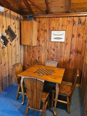 Une pièce en bois avec une table d’échecs et des chaises, un tableau encadré accroché au mur et un plafond en bois rustique.