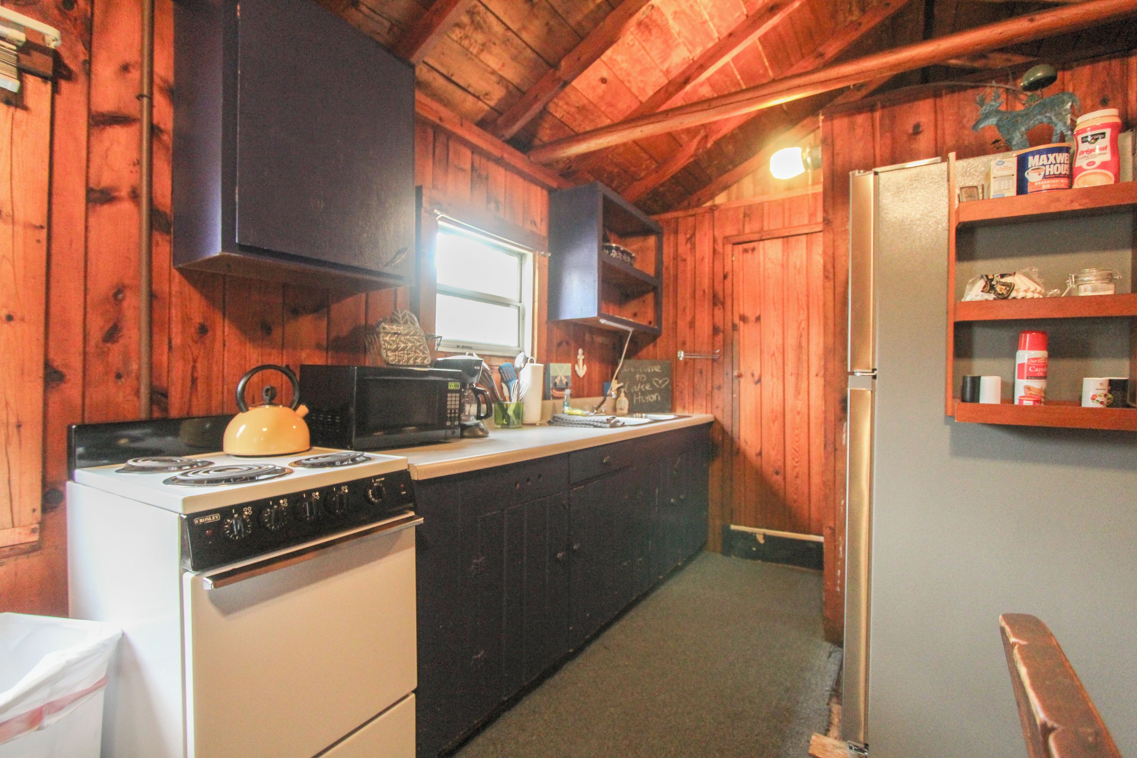 A compact kitchen with wooden walls, a stove, a microwave, and a refrigerator.