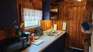 Cocina compacta con paredes de madera, microondas, cafetera y ventana con vistas.