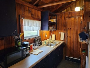 Une cuisine compacte aux murs en bois, équipée d’un four à micro-ondes, d’une machine à café et d’une fenêtre donnant sur un paysage agréable.