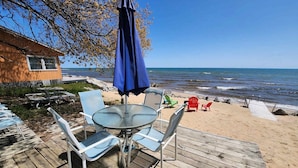 Una terraza frente al mar con una mesa y sillas, una sombrilla azul y vistas al océano.