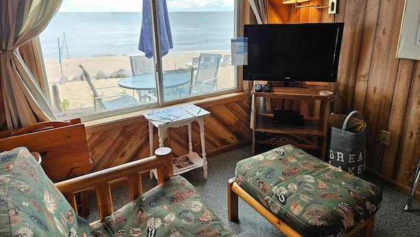 Habitación con televisión, muebles de madera, una mesa con papeles y vistas a la playa.