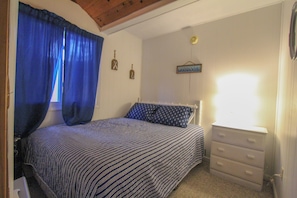 Una camera da letto con un letto, una cassettiera, una finestra con tende e decorazioni alle pareti.
