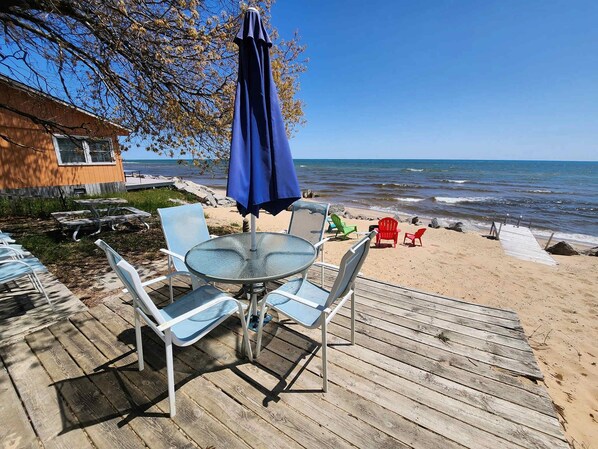 A wooden deck with a round table and chairs, a blue umbrella, and a view of the ocean.