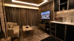 Ein Hotelzimmer mit Sofa, einem kleinen Tisch, einem Fernseher, einer Minibar und einer Küchenzeile.
