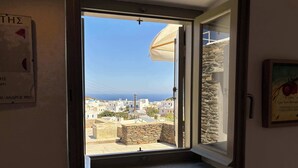 A room with a view of a coastal town, a stone wall, and a door leading outside. - #HH11 Guestroom for two in Katavati (Sifnos)