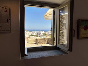 A room with a view of a coastal town, a stone wall, and a door leading outside. - #HH11 Guestroom for two in Katavati (Sifnos)