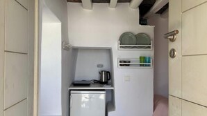 A compact kitchenette with a refrigerator, a kettle, and shelves with dishes and cups. - #HH11 Guestroom for two in Katavati (Sifnos)