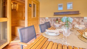 A wooden dining area with a table set for six, chairs, and a stone wall. - 4BR Wellness Villa | Pool, Sauna, Gym (Puerto de la Cruz)