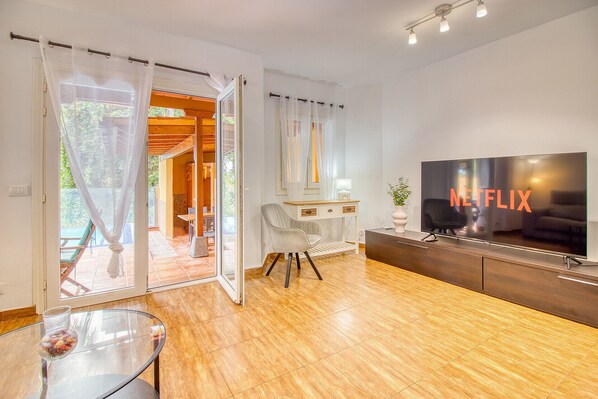 A modern living room with a large flat-screen TV, a glass coffee table, and a sliding glass door leading to an outdoor area.