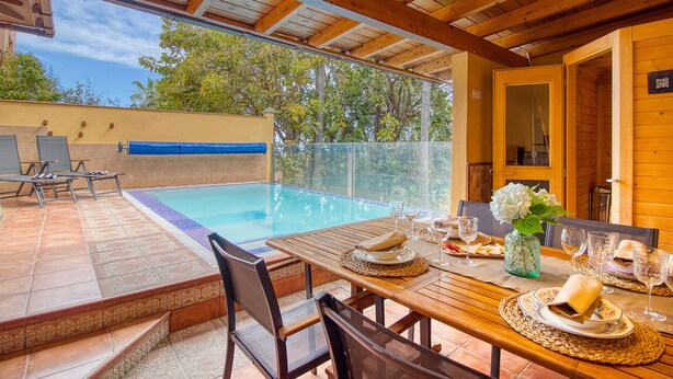 A poolside dining area with a table set for two, a wooden ceiling, and a view of the pool. - 4BR Wellness Villa | Pool, Sauna, Gym (Puerto de la Cruz)