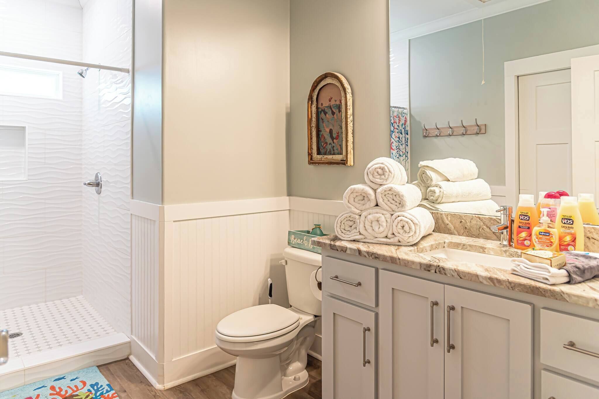 A bathroom with a shower, toilet, and sink. There are towels stacked on the sink counter and toiletries on the counter.