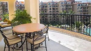 En balkon med et rundt bord og stole, en potteplante og udsigt over et boligområde med bygninger.