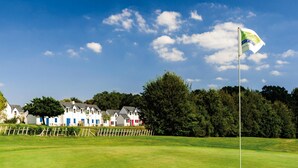 A golf course with a flag, a row of houses in the background, and a clear sky. - Family Cottage for 8 in Morbihan (Queven)