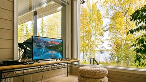 Una habitación con un ventanal grande, un televisor sobre un soporte de madera, un otoman tejido y una alfombra.