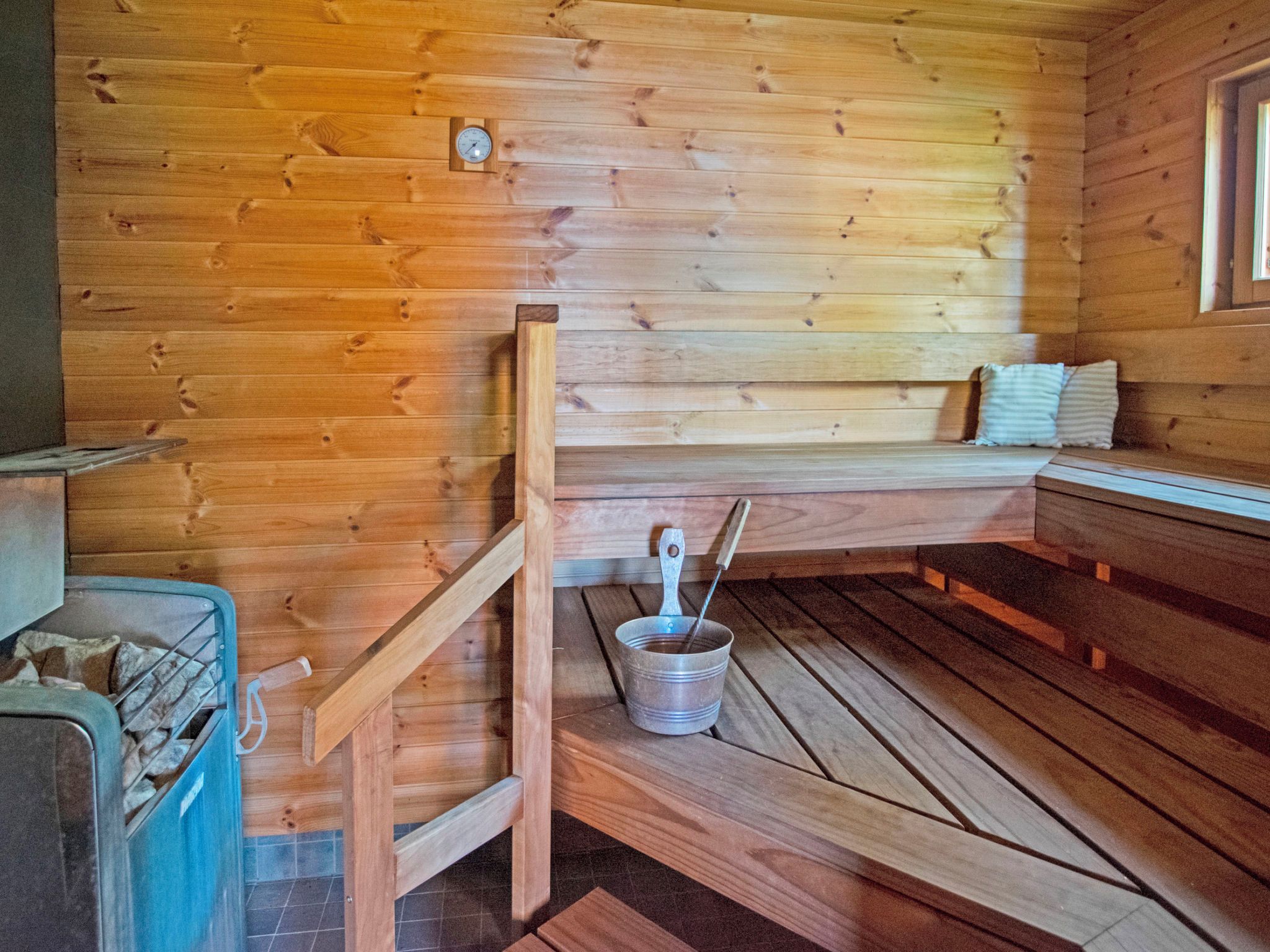 A wooden cabin interior with a wooden bench, a metal bucket, and a wooden ladder.