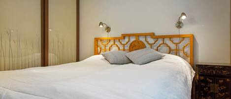 A neatly made bed with a wooden headboard and two wall-mounted lights.
