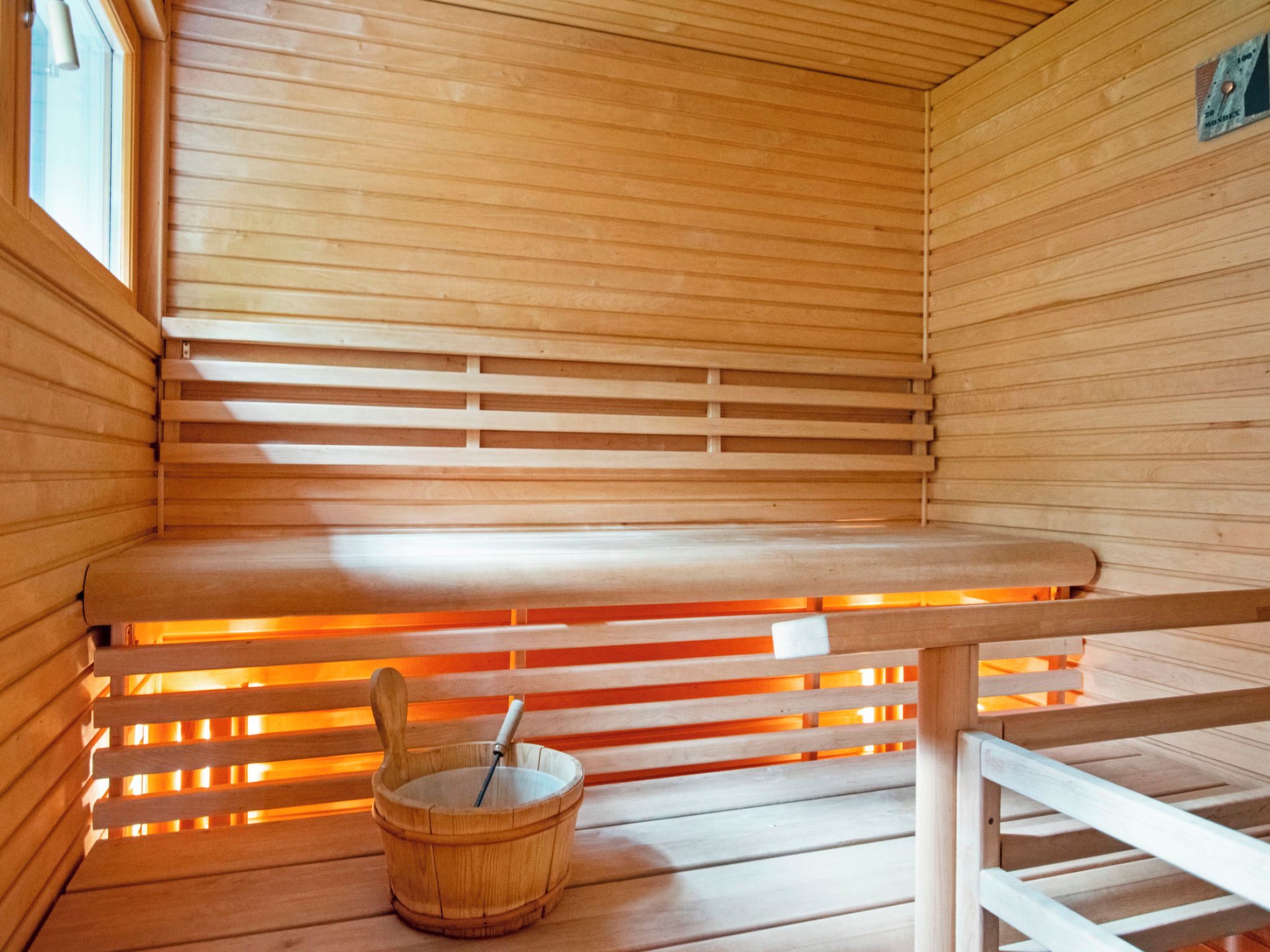 Una sala de sauna con bancos de madera, un calentador para los bancos y un cubo de madera con un palo.