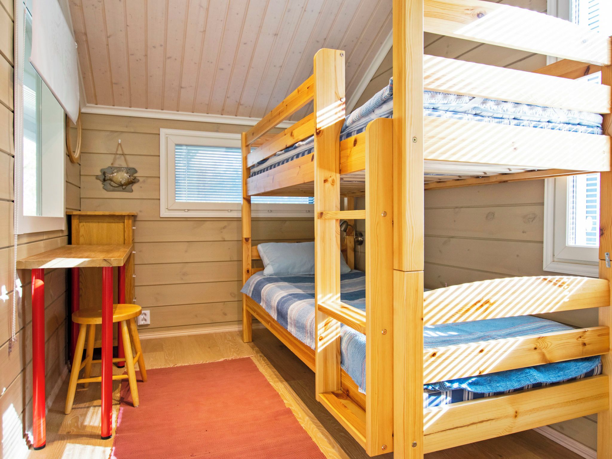 A bunk bed room with a desk and stool, wooden walls, and a window.