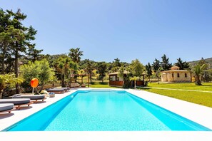 Une piscine avec des chaises longues, un petit bâtiment et de la verdure environnante.