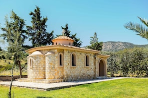 Un bâtiment en pierre doté d’un dôme et de fenêtres en arc de cercle, entouré de verdure et de collines.